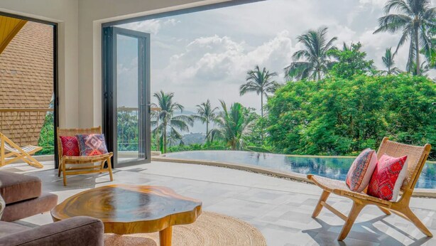 Ein modernes Wohnzimmer mit einem großen Glasfenster, das in einen Poolbereich mit üppiger Vegetation und Palmen führt.