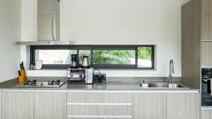 Eine moderne Küche mit einem großen Fenster, einem Gasherd, einer Kaffeemaschine und einem Spülbecken.