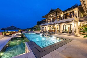 A large, well-lit swimming pool with lounge chairs and a covered area, surrounded by a modern house with a balcony and outdoor seating. - 5-Star traditional Rangsit Villa, 6-bedroom retreat with infinity pool and stunning views (Koh Samui)