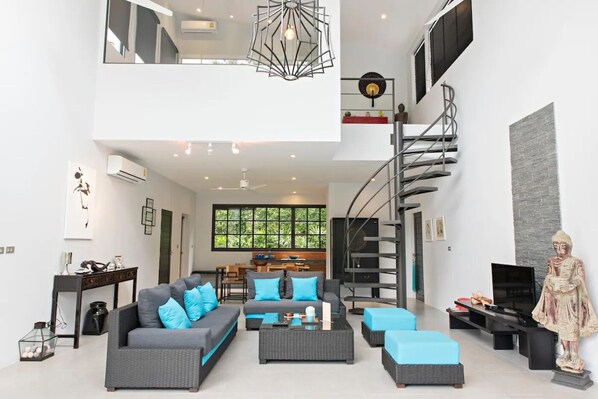 A spacious living area with a high ceiling, a modern staircase, and a statue.