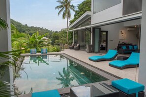 A modern pool area with lounge chairs and a view of a lush garden and hills.