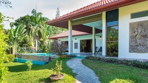 Une maison moderne dotée d’un patio couvert, d’une piscine et d’une végétation luxuriante.