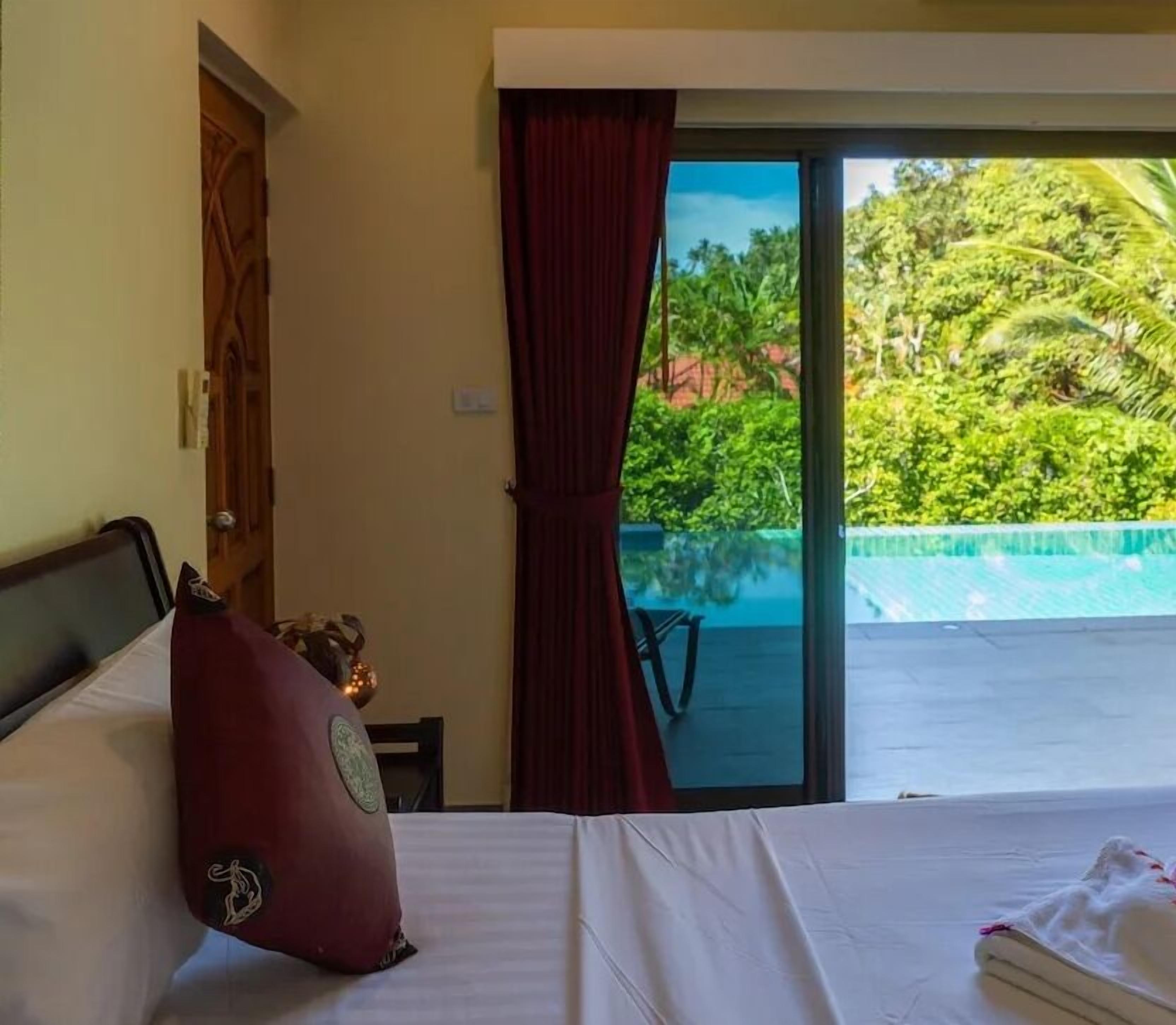Ein Hotelzimmer mit Bett, Fenster mit Blick auf Pool und Grünflächen sowie einer Tür.