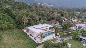 Une maison moderne avec une piscine, entourée d’une végétation luxuriante et de palmiers.