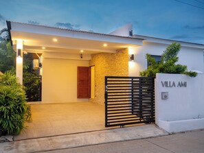 A modern villa entrance with a gated driveway, a wooden door, and a sign reading 'VILLA AMI'.