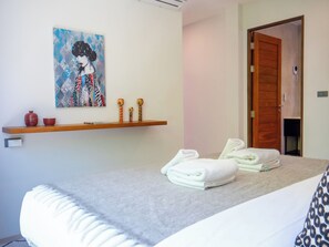 A bedroom with a bed, a wooden shelf with decorative items, a painting, and a door. - Luxury 3-bedroom villa in BangRak with private pool, and terrace for starry nights (Tambon Bo Put)