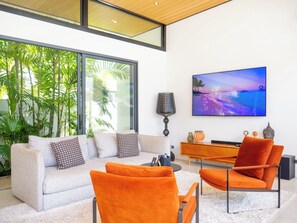 A modern living room with a sofa, orange chairs, a TV, and a wooden cabinet.
