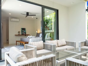 A modern hotel room with a glass door leading to a balcony, a bed with pillows, a bedside table, and a ceiling fan. - Luxury 3-bedroom villa in BangRak with private pool, and terrace for starry nights (Tambon Bo Put)