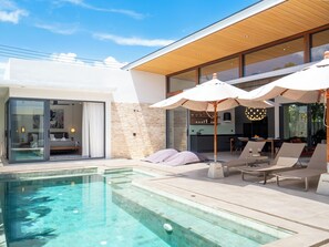 A modern house with a swimming pool, outdoor seating, and a kitchen visible through large windows.