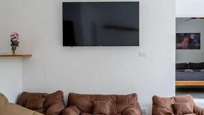 A modern living room with a large flat-screen TV mounted on the wall, a brown leather sofa, and a small side table with a vase of flowers.