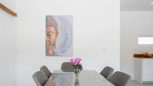 A modern dining area with a glass table, woven chairs, and a Buddha painting on the wall.