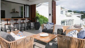 A modern outdoor seating area with wicker furniture, a wooden table, and a bar area with stools.