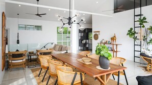 A spacious dining area with a long wooden table, wicker chairs, and a central potted plant.