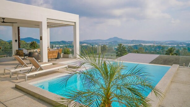 A rooftop pool with lounge chairs, a covered seating area, and a view of distant mountains.