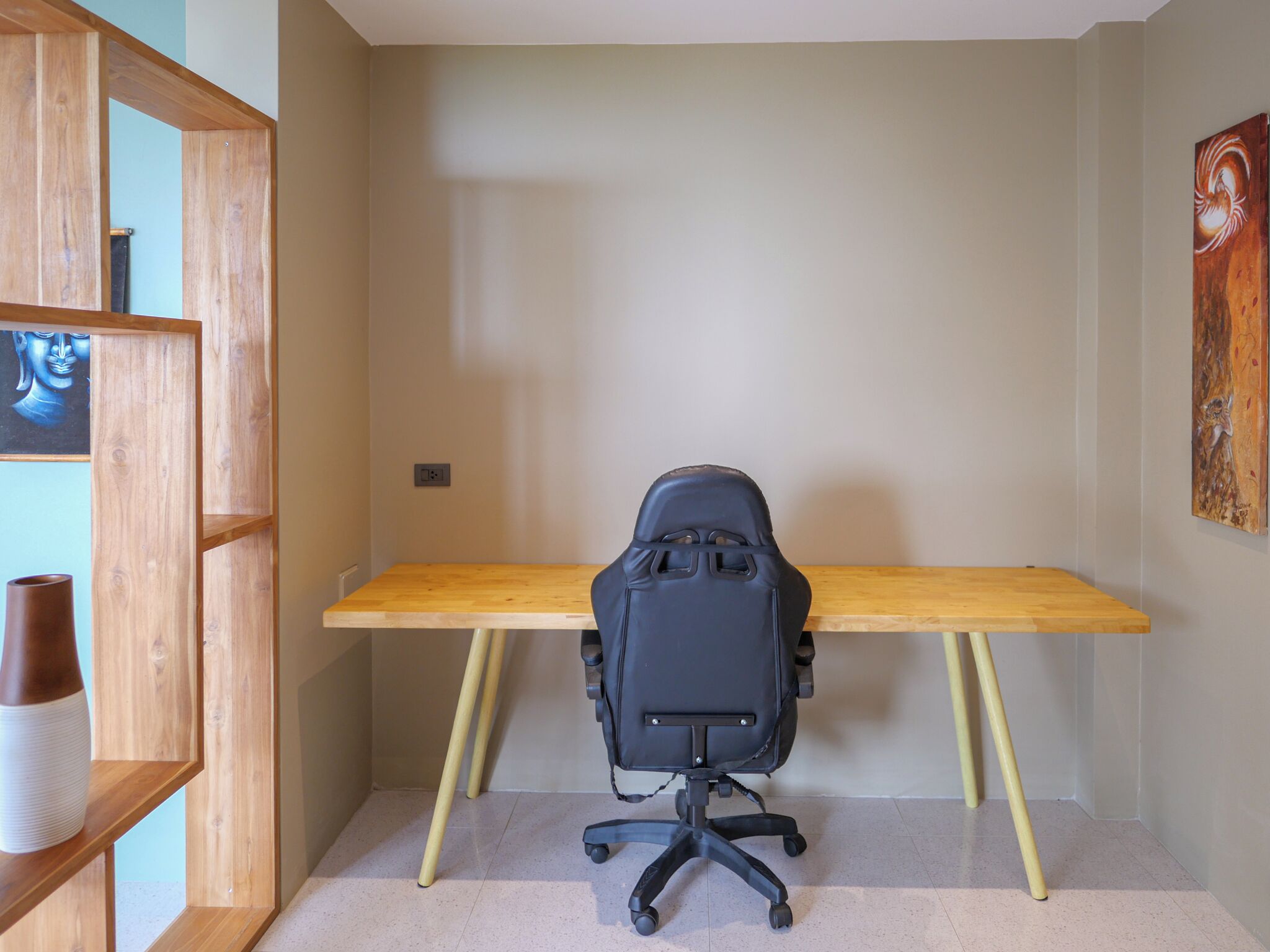 Een werkplek met een houten bureau, een zwarte bureaustoel en een plank met vazen.