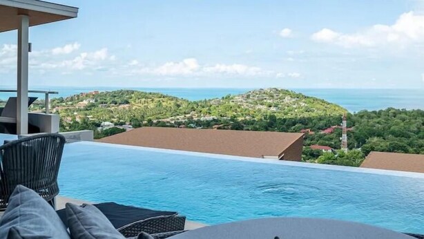 Una piscina privada con vistas a una colina verde y al mar.