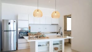 A modern kitchen with white cabinetry, a stainless steel refrigerator, a built-in oven, and a central island with a woven light fixture.