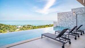 A modern infinity pool with lounge chairs, a stone wall, and a view of the ocean. - Luxurious 3 king-suite villa in Plai Laem Soi 8 with private pool, sea views, and WiFi (Koh Samui)