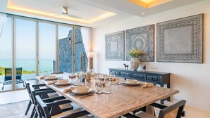 A dining area with a large table set for six, a view of the sea through large windows, and decorative wall art. - Luxurious 3 king-suite villa in Plai Laem Soi 8 with private pool, sea views, and WiFi (Koh Samui)