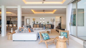 A spacious living area with a sofa, chairs, and a dining table. There is a kitchen in the background and a large window on the right. - Luxurious 3 king-suite villa in Plai Laem Soi 8 with private pool, sea views, and WiFi (Koh Samui)