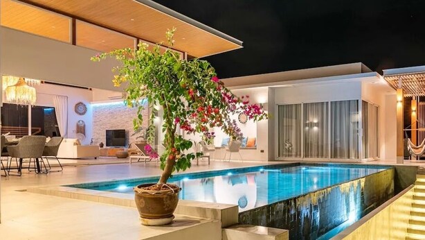 Ein moderner Poolbereich mit Glasveranda, Essbereich mit Stühlen und eine Treppe zu einer überdachten Terrasse.
