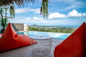 An infinity pool with a clear view of the landscape, surrounded by red seating and a decorative metal table.