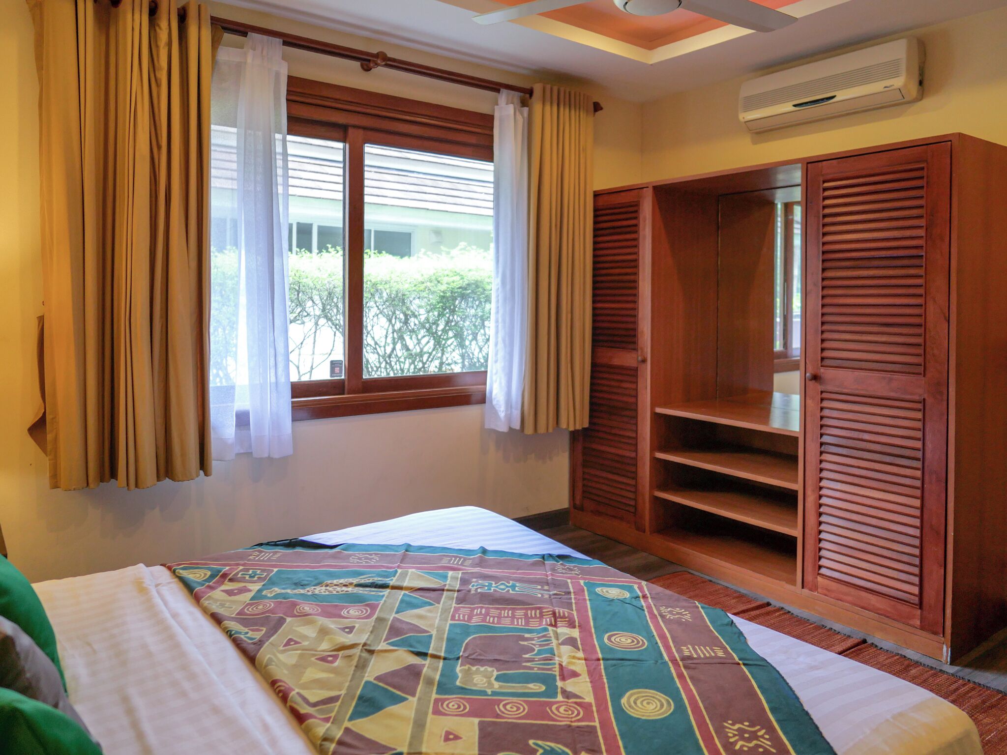 A bedroom with a bed, a wardrobe, a window with curtains, and an air conditioning unit.
