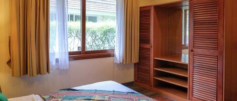 A bedroom with a bed, a wardrobe, a window with curtains, and an air conditioning unit.