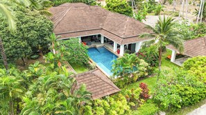 A house with a swimming pool surrounded by lush greenery and palm trees.