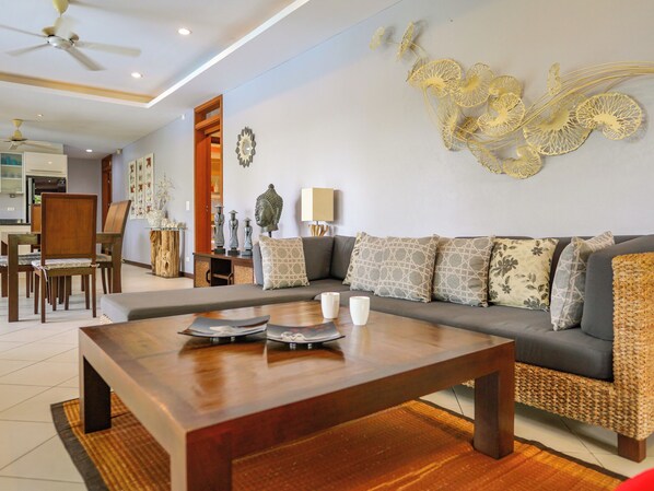 A modern living room with a wooden coffee table, a grey sofa with patterned cushions, and a decorative wall piece.
