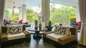 Une pièce meublée de mobilier en osier, avec une table ronde et une vue sur une piscine et un espace verdoyant.