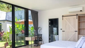 A modern bedroom with a large bed, a desk with a chair, a sliding door closet, and a view of greenery outside. - Modern 2-bedroom oasis with private pool, garden, and dedicated workspace, ideal for families (Tambon Mae Nam)