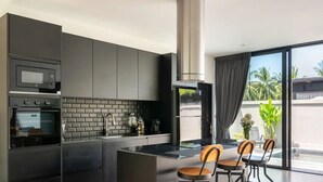 A modern kitchen with a central island, built-in appliances, and a large window offering a view of palm trees. - Modern 2-bedroom oasis with private pool, garden, and dedicated workspace, ideal for families (Tambon Mae Nam)