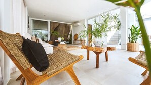 A modern living room with wicker furniture, a large plant, and a staircase leading to an upper level.
