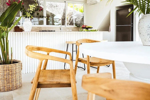 A modern kitchen with a white countertop, wooden chairs, and a large window with a view of greenery.