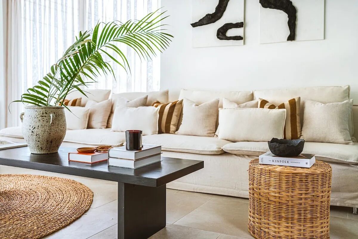 Un salon avec un canapé, une table basse, un tabouret en osier et une plante en pot.