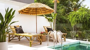 A poolside area with two bamboo lounge chairs, a woven umbrella, and a small pool.