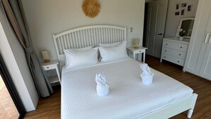 A neatly made bed with white bedding and pillows, a bedside table with a lamp, and a wall-mounted air conditioning unit. - Stylish 2-Bedroom VIlla in Plai Laem, Private Pool with Jacuzzi, Close to Attractions (Koh Samui)