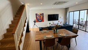 A modern living room with a wooden staircase, a dining area with a table set for two, a large TV mounted on the wall, and a balcony with outdoor seating. - Stylish 2-Bedroom VIlla in Plai Laem, Private Pool with Jacuzzi, Close to Attractions (Koh Samui)