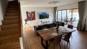 A modern living room with a dining area, wooden flooring, a staircase, and a large window with a view.