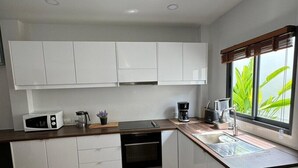 A modern kitchen with white cabinets, a built-in oven, a coffee maker, and a window with a view of greenery.