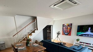 A modern living room with a dining area, a blue sofa, wooden flooring, a staircase, and a mounted TV.
