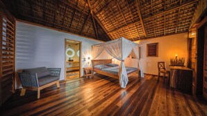 Una habitación con piso de madera, una cama con dosel, un sofá, una mesita y una silla.