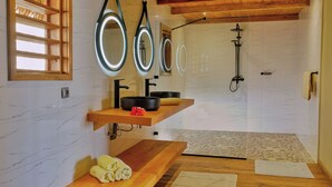 Un baño moderno con tocador de madera, un espejo grande, zona de ducha y estante de madera con toallas.