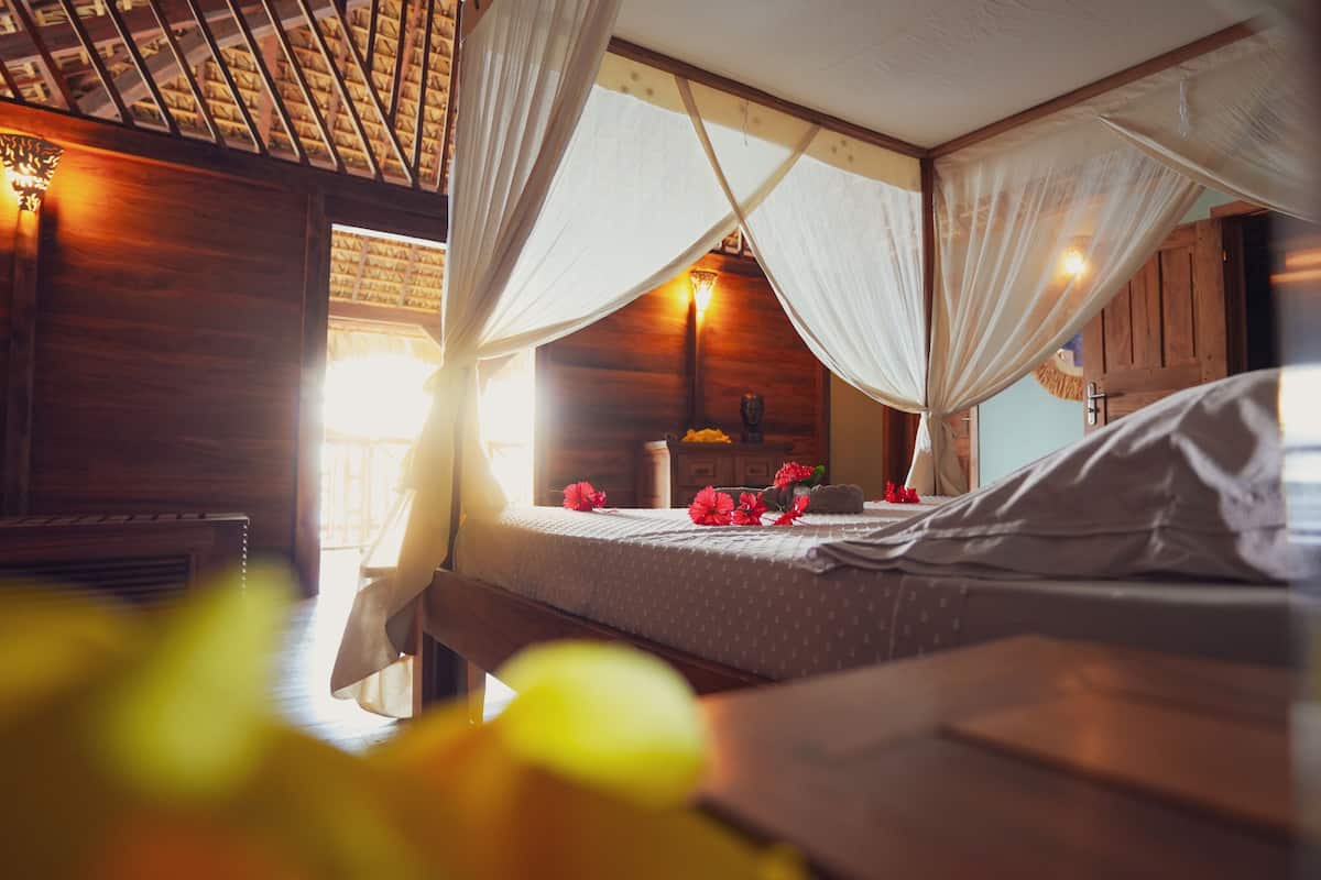 Quarto de madeira com uma cama, mesa de cabeceira e janela com cortinas.