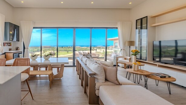 Un salon moderne avec un grand canapé, une table à manger et des chaises, un téléviseur et une vue sur l’océan.