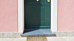 Eine grüne Tür mit zwei Messinggriffen, einem weißen Rahmen und einer schwarzen Leuchte darüber.