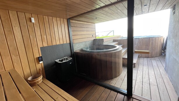 Una terraza de madera con un jacuzzi, un banco y un pequeño contenedor de basura.