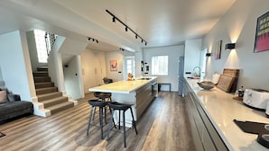 Una cocina moderna con una isla central, taburetes de bar, horno empotrado y un refrigerador.