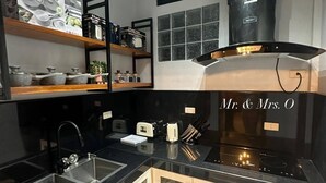 A modern kitchen with black countertops, stainless steel appliances, and a built-in oven. There are wooden shelves above the sink and a window with a view of the city. - Micasa Mabini (Puerto Princesa)